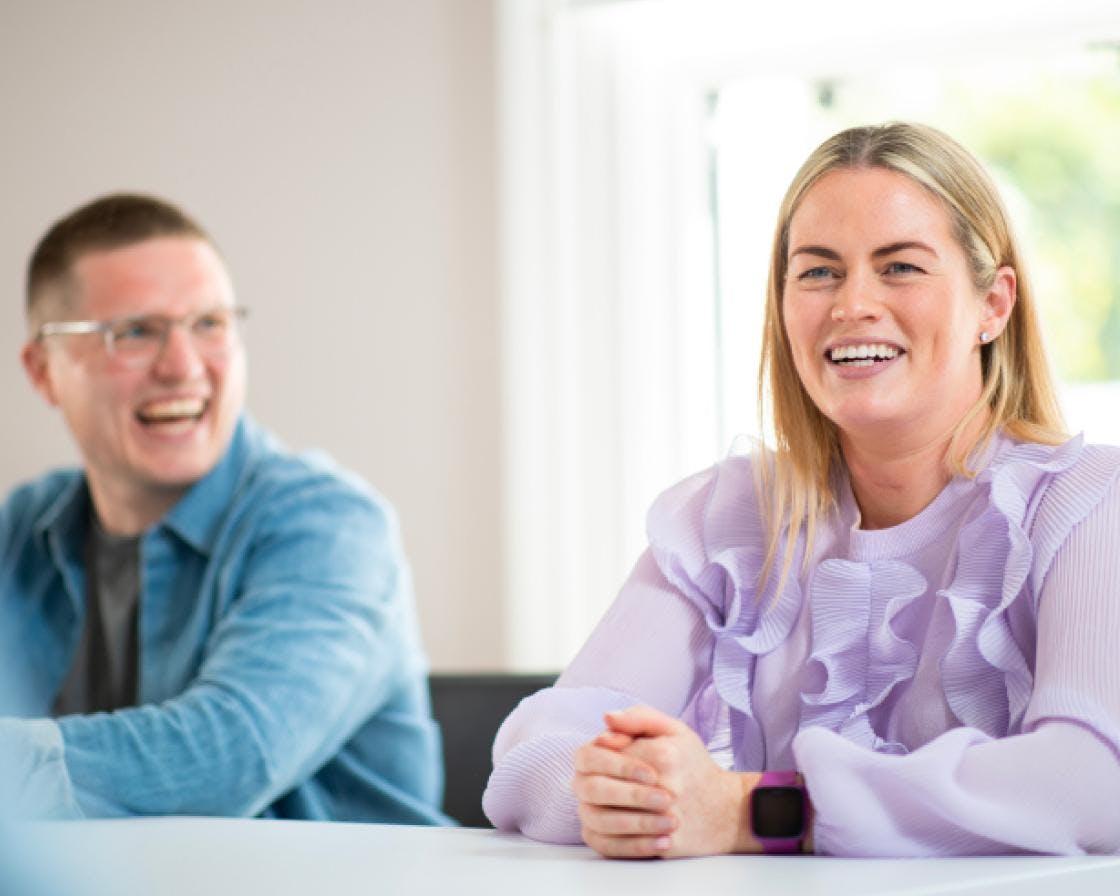 Ein Mann und eine Frau sitzen lachend und lächelnd an einem Schreibtisch